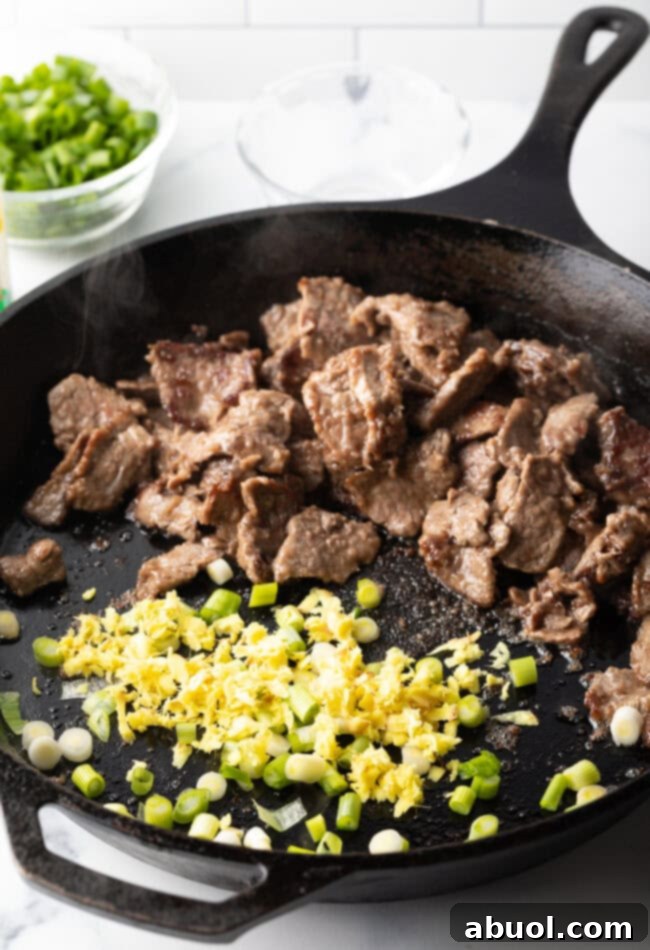 Searing sliced flank steak with garlic and scallion whites in a hot skillet.