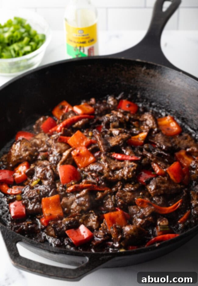 Sliced steak and vibrant red bell peppers stir-fried together in a skillet, coated in a savory sauce.