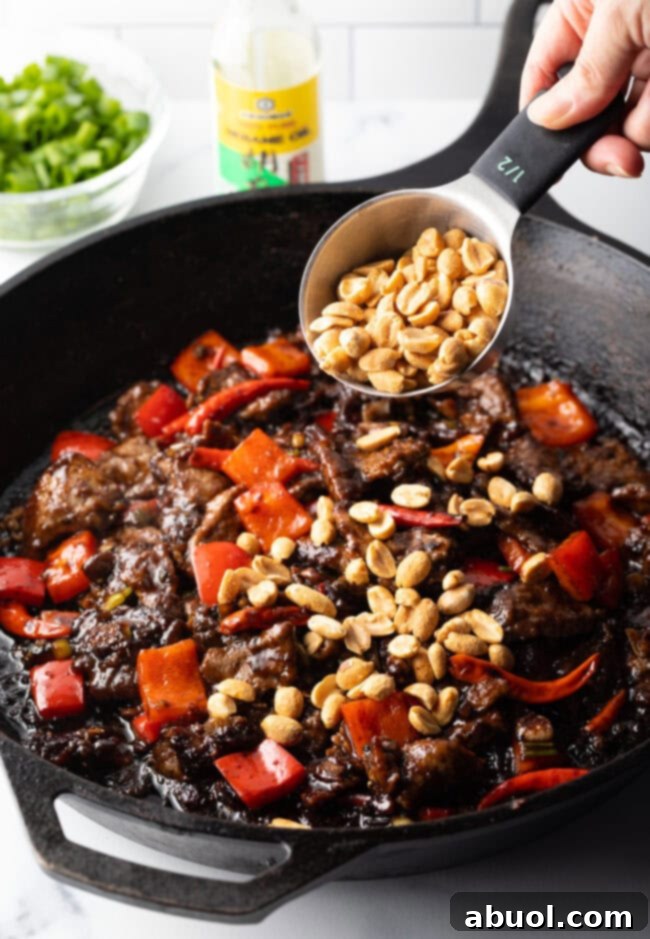 A hand adding chopped roasted peanuts into the skillet with the cooked Kung Pao Beef.