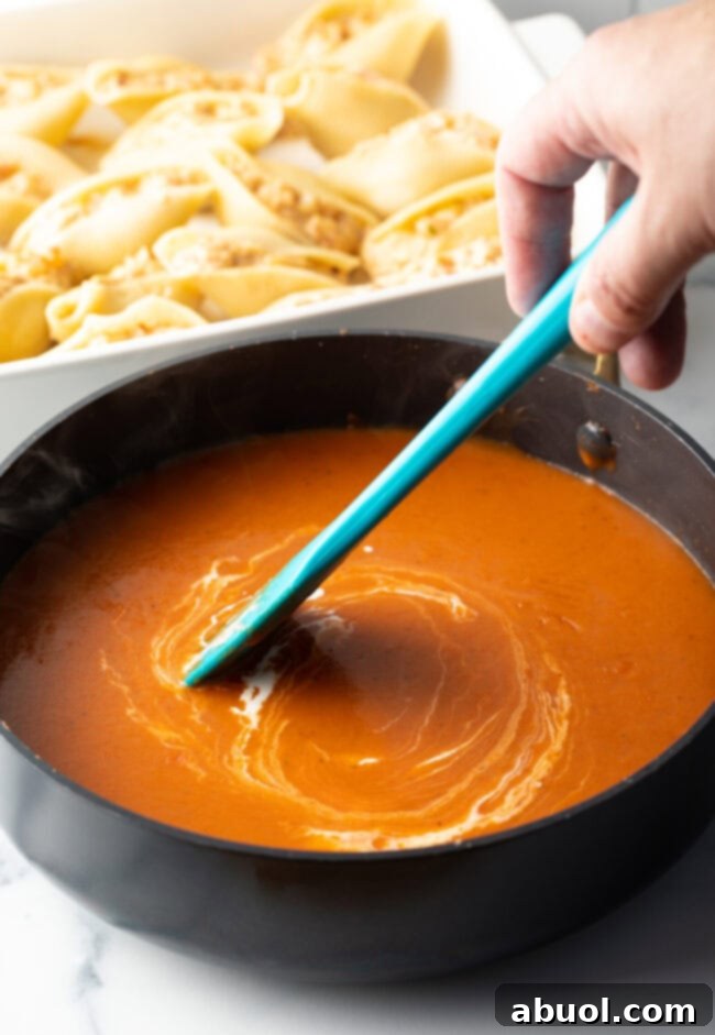 A hand with a blue spatula stirring a cheesy mixture in a saucepan, highlighting the creamy texture.