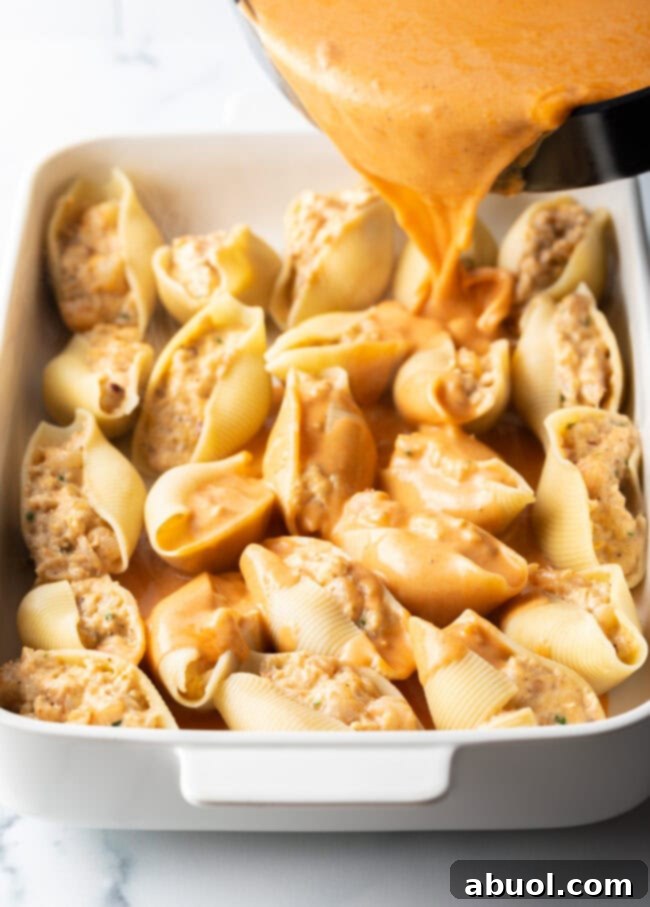 Pouring rich seafood sauce over the white baking dish filled with stuffed pasta shells.