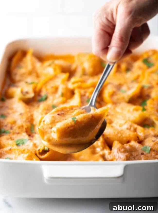 A hand with a metal spoon, showcasing a perfectly scooped portion of seafood stuffed pasta to the camera.