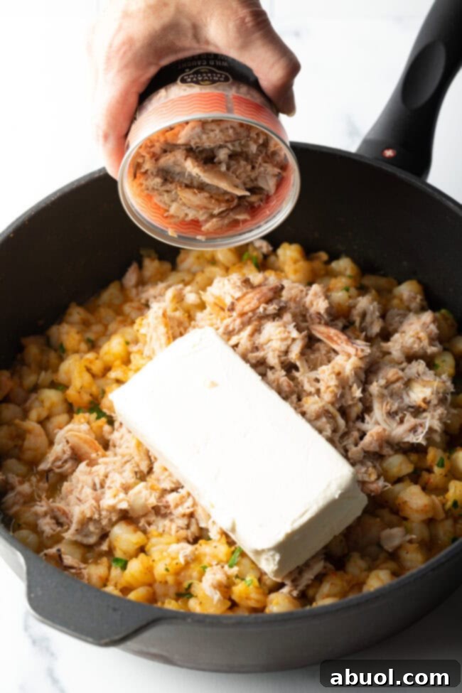 Adding cream cheese and other ingredients to the skillet with cooked seafood for the filling.