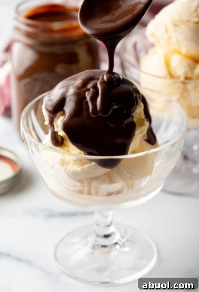 Spoon drizzling the homemade hotfudge sauce over a glass bowl of vanilla ice cream.