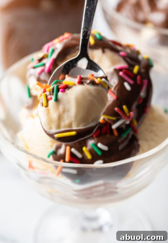 Metal spoon with scoop of vanilla ice cream, chocolate sauce, and sprinkles.