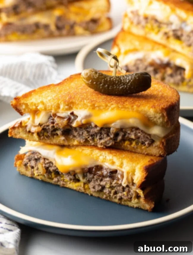 Two halves of a patty melt stacked on top of each other, held together by a wood skewer with a small pickle on top.