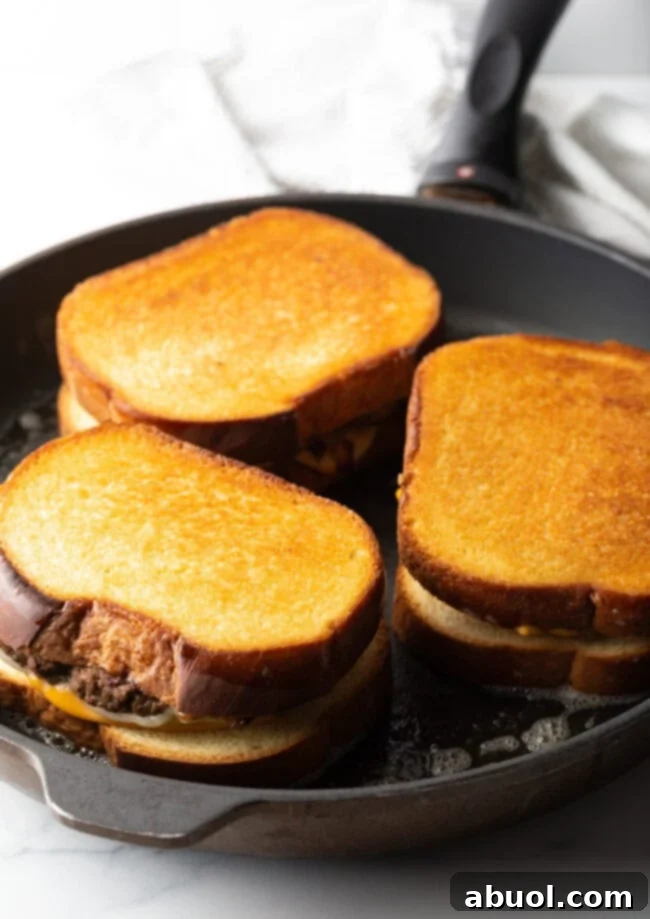 Three patty melts being toasted in a large skillet, with bread golden brown.