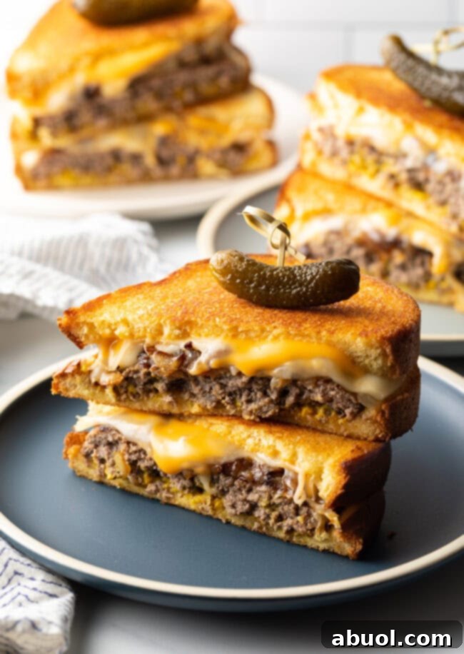Two halves of a patty melt stacked on top of each other, garnished with a pickle. A perfect diner-style meal.