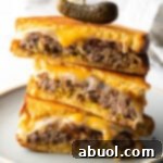 Three pieces of two patty melts stacked on top of each other. A wood skewer with small pickle is going through the top of the sandwich stack.