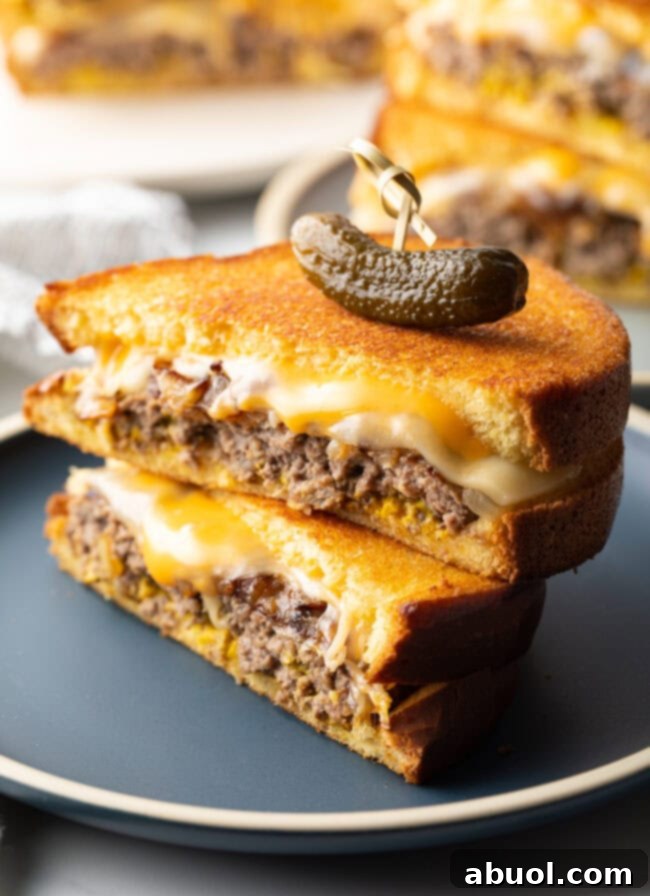 Close-up view of two halves of a perfectly toasted patty melt, showing the melted cheese, caramelized onions, and juicy patty.