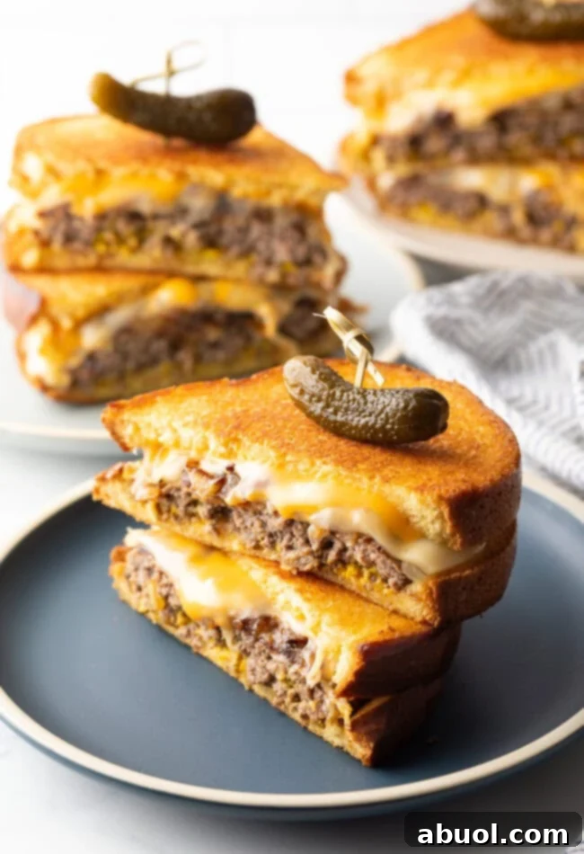 Two halves of a patty melt stacked on top of each other, ready to be served. A small pickle skewer holds them together.
