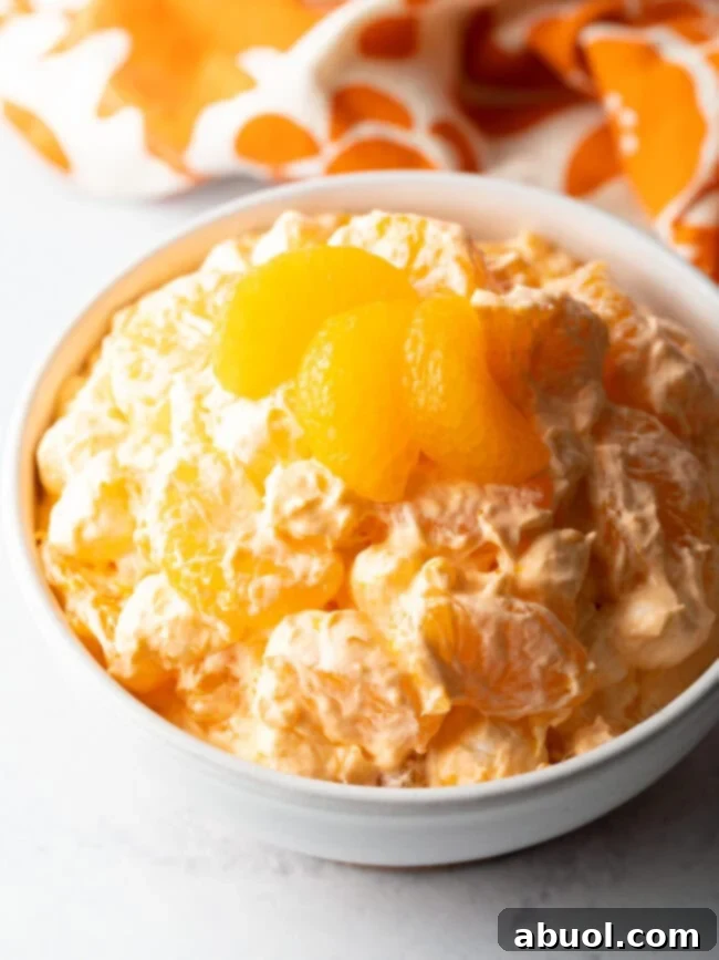 Top-down view of a vibrant Mandarin Orange Fluff Salad in a white bowl, elegantly garnished with three fresh orange slices.