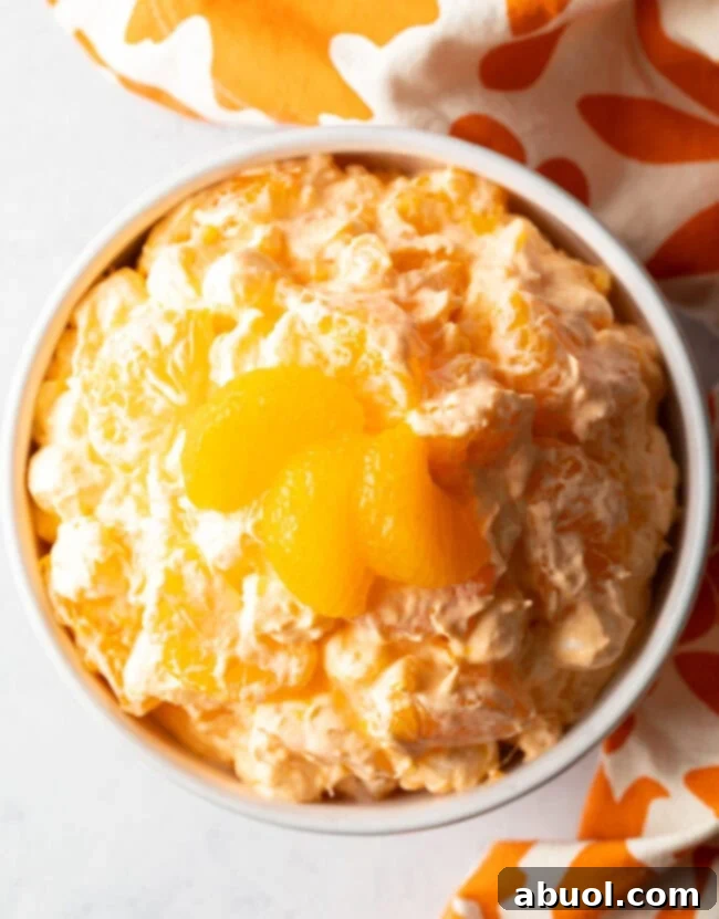 Top-down view of Mandarin Orange Fluff Salad presented in a white serving bowl, garnished with three fresh orange slices for a vibrant presentation.
