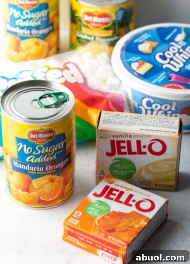 Collection of key ingredients for Orange Fluff Salad: Cans of mandarin oranges and crushed pineapple, boxes of orange Jell-O gelatin and instant vanilla pudding mix, a tub of Cool Whip, and a bag of mini marshmallows, all neatly arranged for preparation.