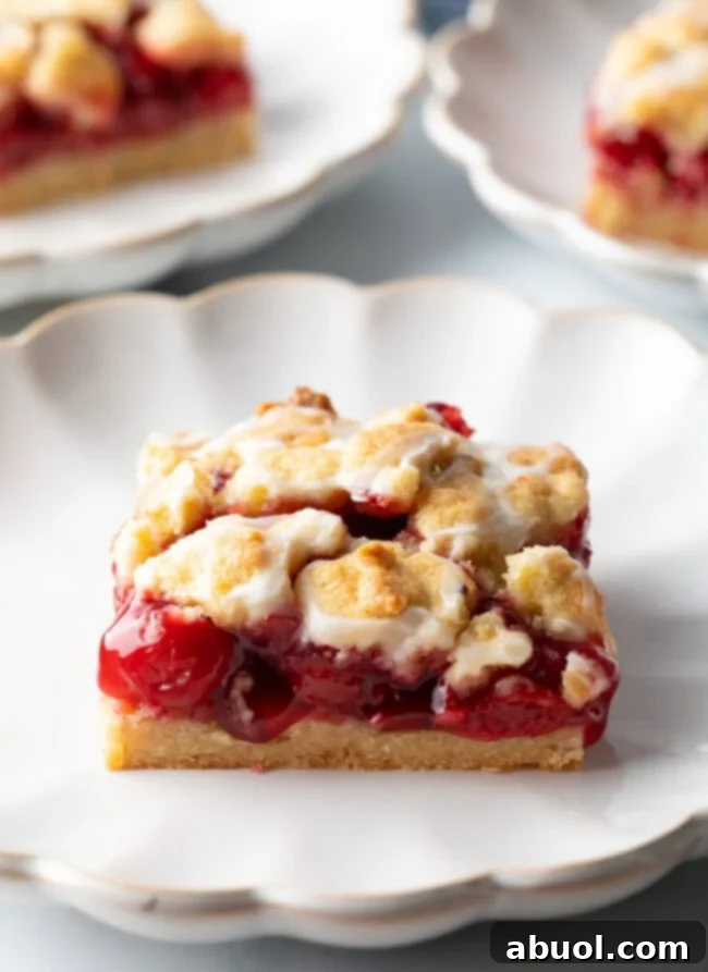A square piece of cherry pie bar, glistening with glaze, resting on a pristine white scalloped plate.