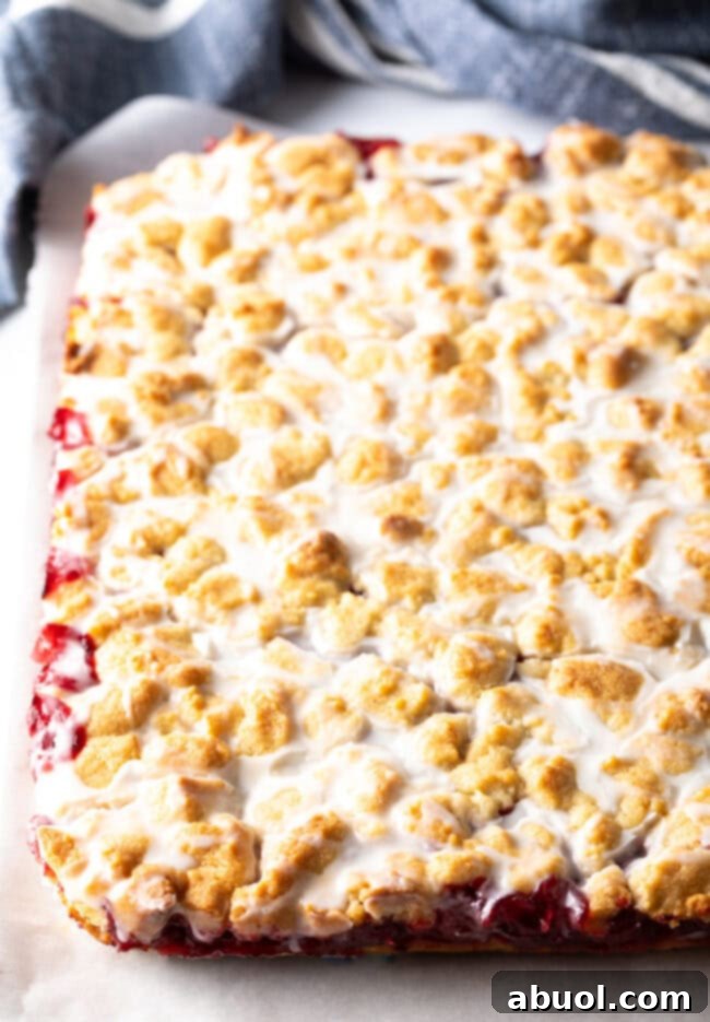 A baked pan of cherry pie bars, showcasing the golden-brown crumb topping and the slight sheen of a sugar glaze.