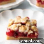 A square piece of cherry pie bar on a white scalloped plate, ready to be enjoyed.
