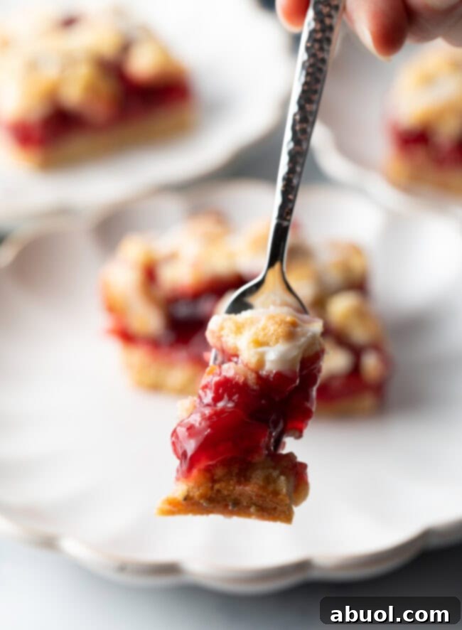 A metal fork poised to take a bite of a cherry pie bar, highlighting the gooey cherry filling and crumbly crust texture.