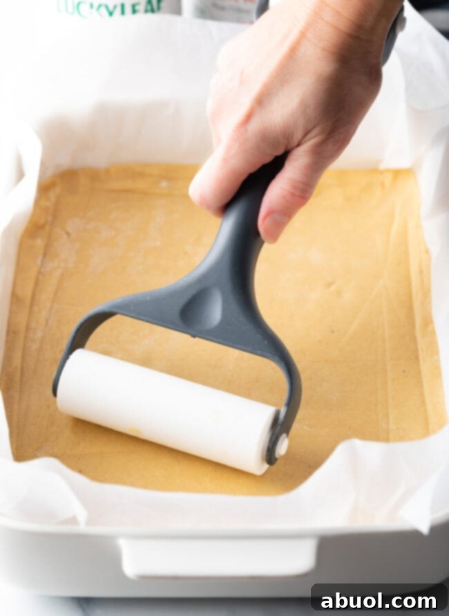 A hand using a pastry roller to gently smooth out a rectangle of pie dough into an even layer within a baking pan.