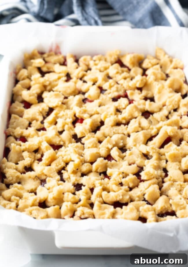 A baking pan filled with a generous layer of cherry filling, topped with scattered raw pie dough pieces, ready for baking.