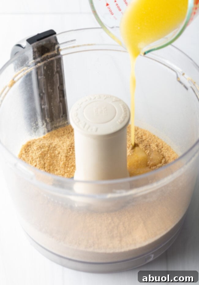 Adding melted butter to the crushed graham crackers in a food processor.