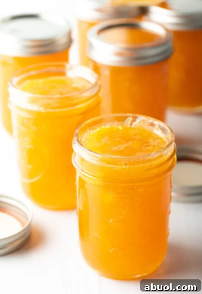 Multiple jars of golden peach preserves without lids, showcasing their rich color and appealing texture. Ready to be sealed and enjoyed.