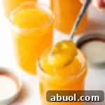 Close-up of a jar of homemade peach jam with a metal spoonful held to camera, tempting and delicious.