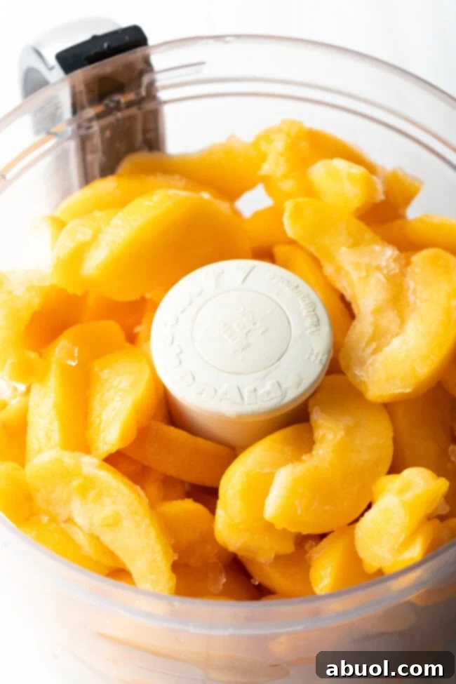Fresh peach slices being added to a food processor, ready for the initial mashing step in making preserves.