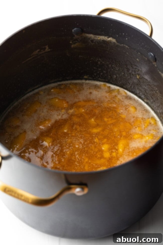 The fruit mixture actively cooking down in a large black pot, with steam gently rising, indicating the preserves are nearing completion.