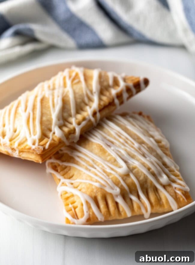 Homemade Peach Toaster Pastries 2 Two golden-brown homemade peach pop tarts, freshly baked and ready to be glazed, resting against each other on a pristine white plate.