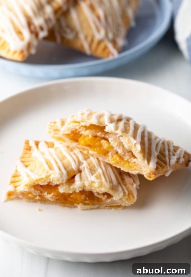 Homemade Peach Toaster Pastries 14 A peach pop tart, perfectly baked and sliced open to show its rich, warm peach filling, presented on a white plate with one half leaning against the other.