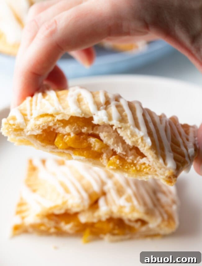 Homemade Peach Toaster Pastries 15 A hand holds half of a freshly baked peach hand pie towards the camera, showcasing the delicious, golden peach filling inside.