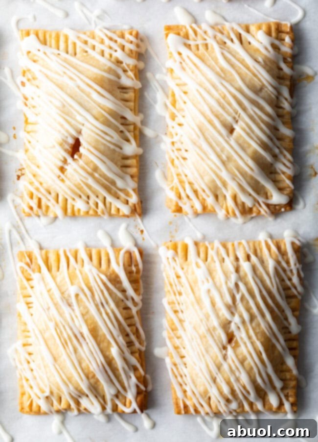 Homemade Peach Toaster Pastries 4 Four finished homemade peach hand pies, beautifully drizzled with white icing, arranged on a rustic wooden board.
