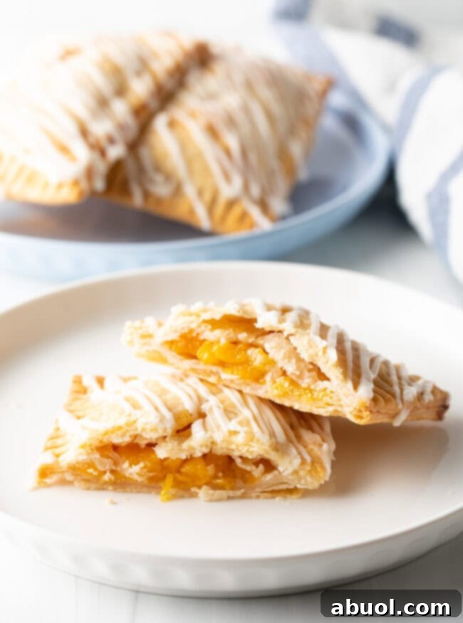 Homemade Peach Toaster Pastries 5 A perfectly baked peach pop tart, cut in half to reveal its warm, fruity peach filling, with one half gently leaning on the other on a white plate.