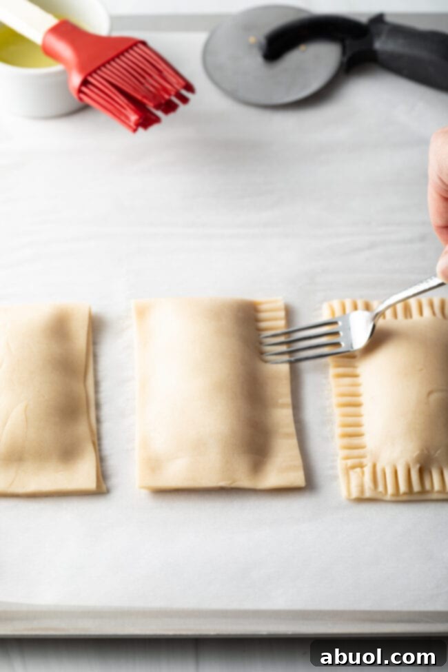 Homemade Peach Toaster Pastries 10 A hand gently crimping the edges of an unbaked peach hand pie with a fork, ensuring a tight seal and decorative finish.