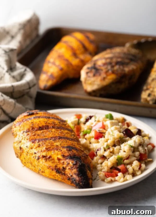One whole chicken breast, perfectly seasoned and grilled, presented on a pristine white plate next to a vibrant serving of fresh bean salad.