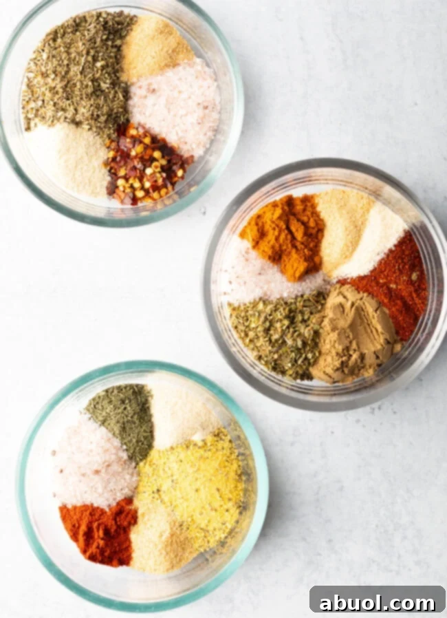 Top down view of three rustic bowls, each containing a different vibrant blend of homemade chicken seasoning.