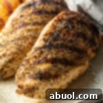 Top down view two whole chicken breasts seasoned and grilled, resting on a white plate.