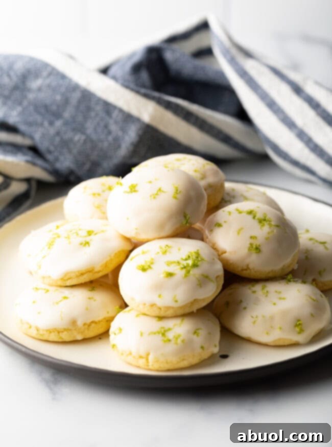 A pristine white plate generously piled with glossy, glazed key lime cookies, inviting a sweet, citrusy indulgence.
