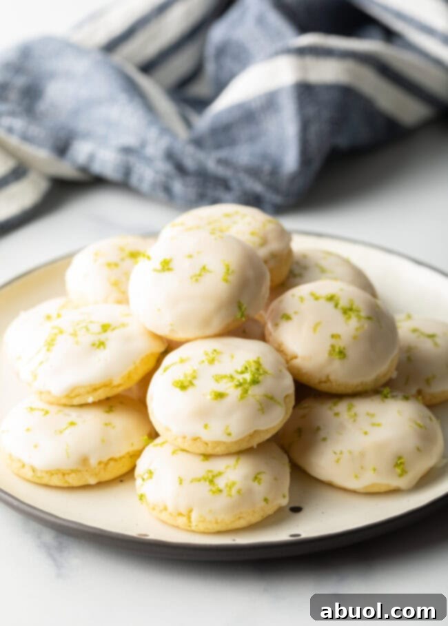 A pristine white plate generously piled with glossy, glazed key lime cookies, inviting a sweet, citrusy indulgence.