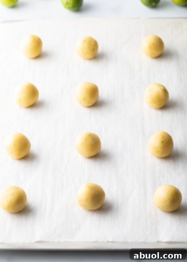 Neatly arranged, unbaked balls of cookie dough are lined up on parchment paper, awaiting their transformation in the oven.