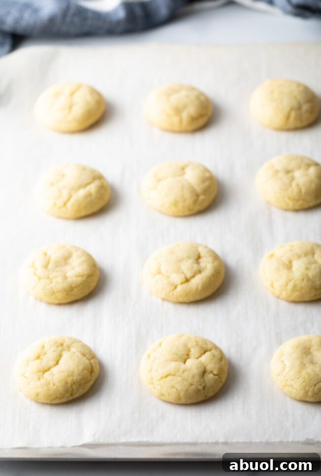 A sheet of parchment paper holds perfectly baked, soft cookies, golden around the edges and ready for glazing.