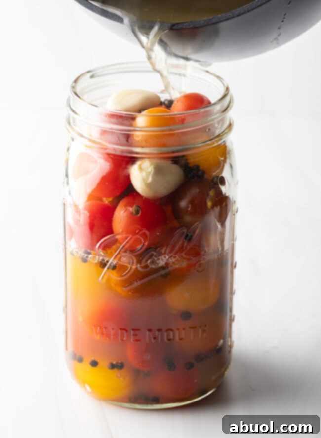 Adding pickling liquid to large glass jar filled with small red and yellow tomatoes.