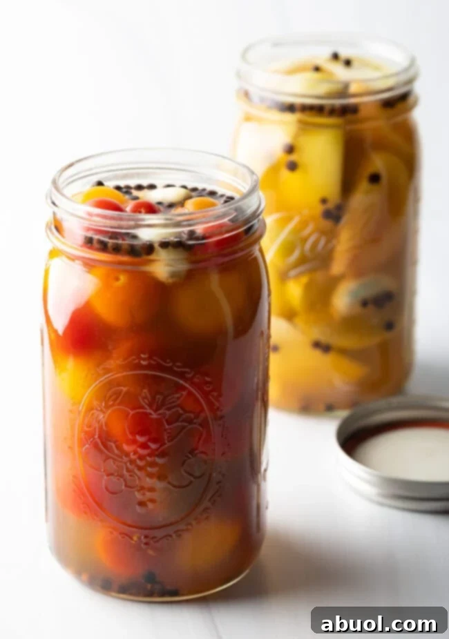 Marinated pickled cherry tomatoes in a large glass jar in the foreground. Marinated pickled green tomatoes in a large glass jar in the backrground.