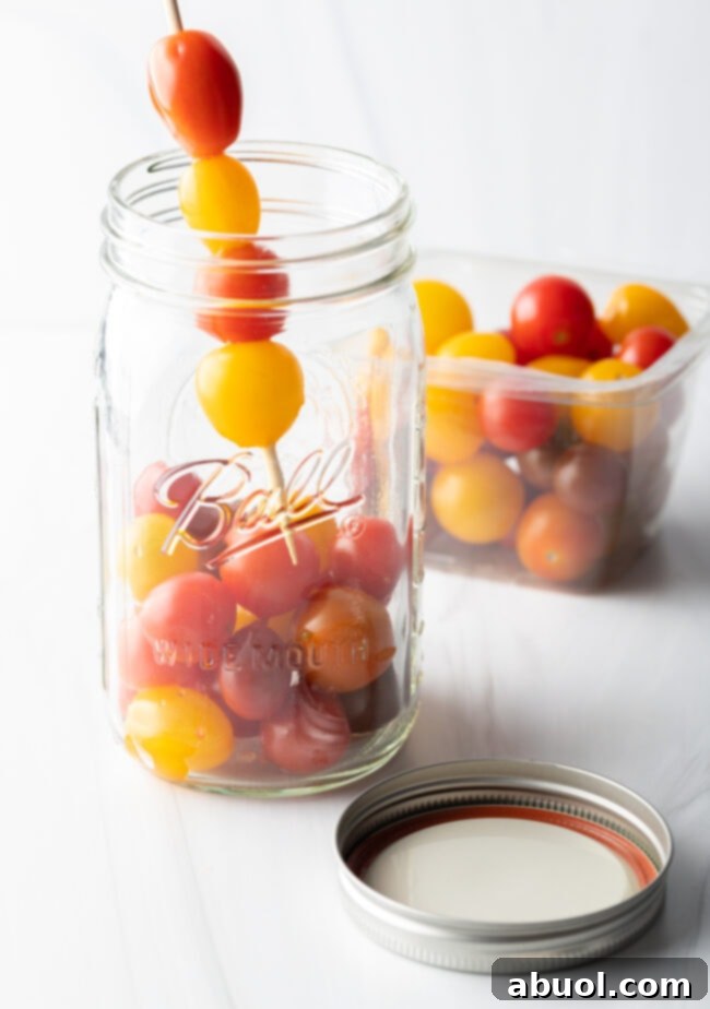 Adding small yellow and red cherry tomatoes to a large glass ball jar.