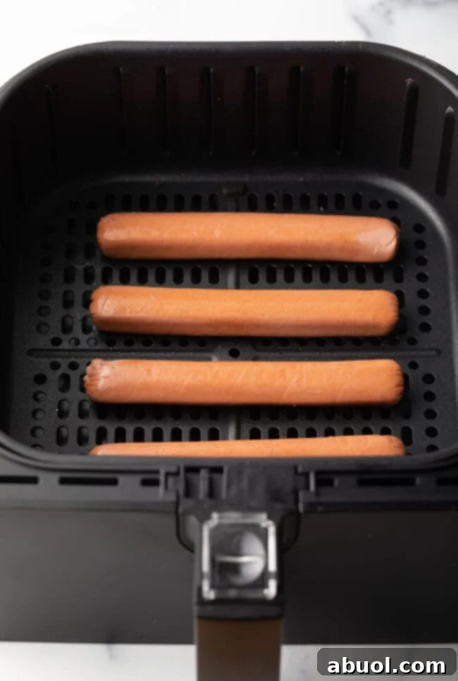 A top-down view shows four raw hot dogs neatly arranged in an air fryer basket, ready for cooking.