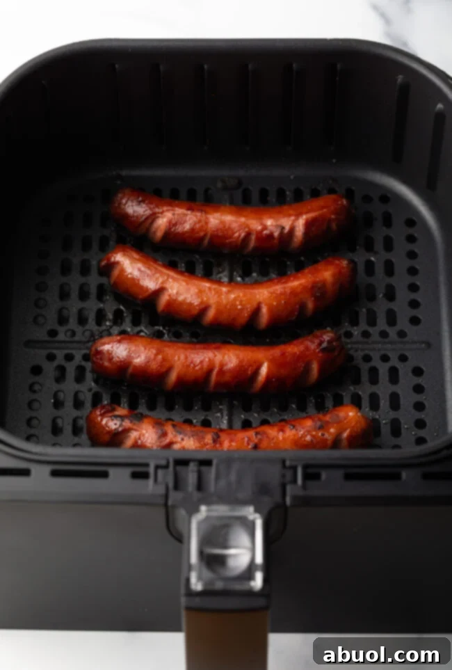 Close-up of perfectly cooked, dark brown hot dogs resting in the air fryer basket, showing their crispy texture.