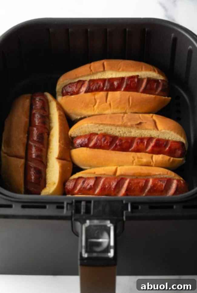 Four hot dogs nestled in their buns, toasting to golden perfection within an air fryer basket.