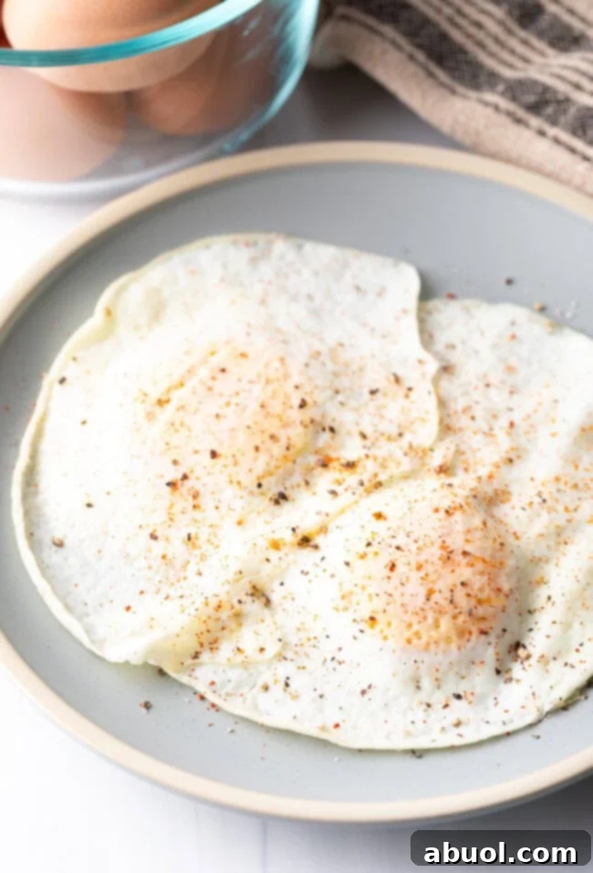 Two cooked eggs over easy on a light blue plate, sprinkled with spices.
