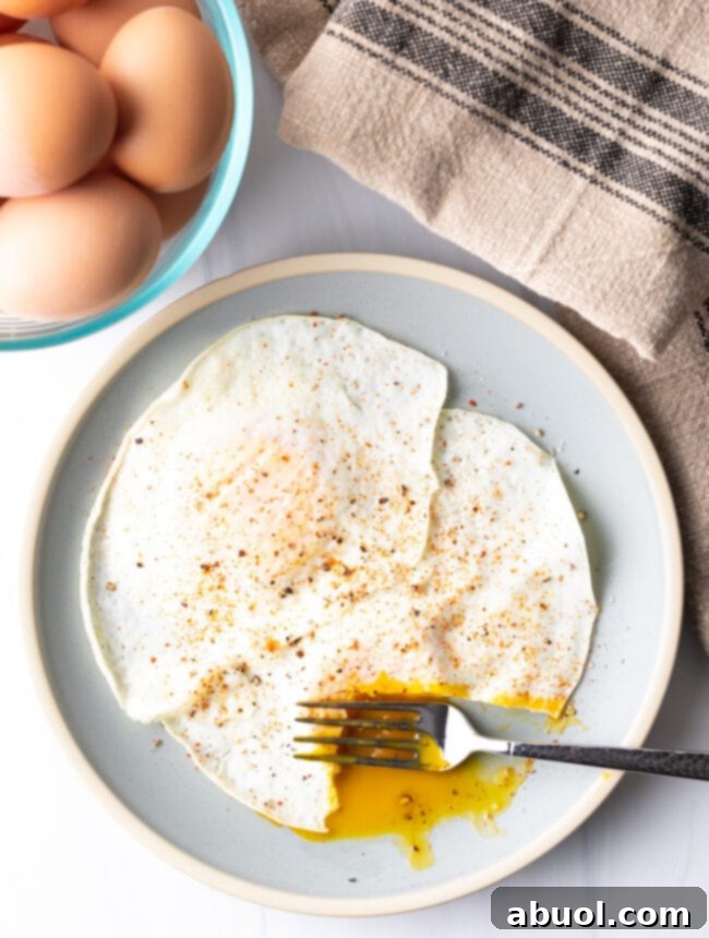 Fork cutting into th soft yolk of a gently over easy fried egg, on a light blue plate.
